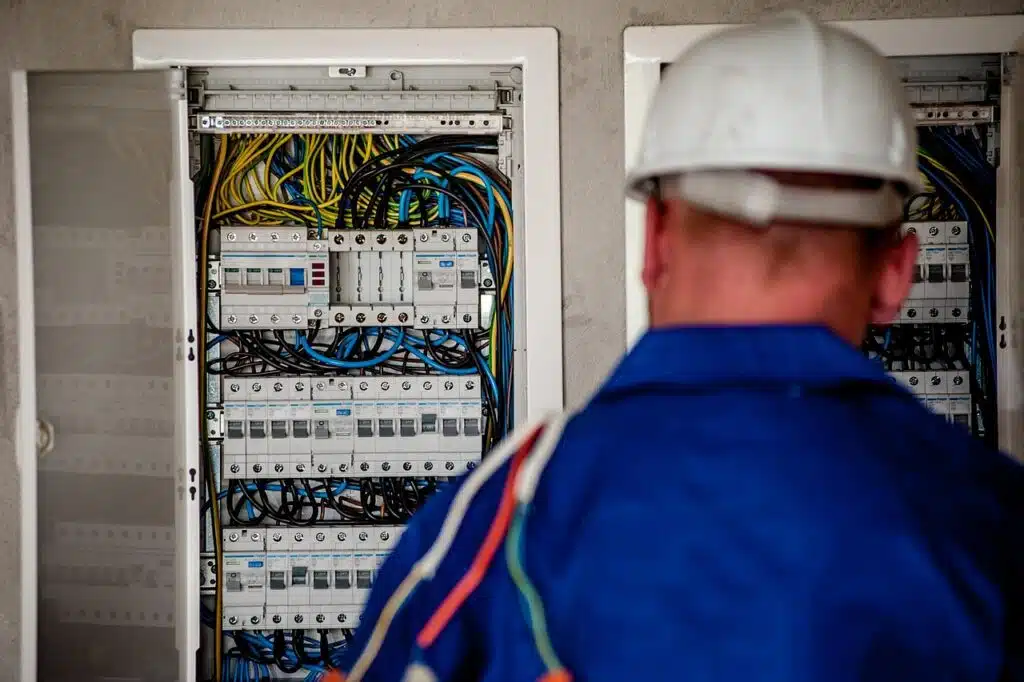 Elektriker mit Schutzhelm vor einem geöffneten Stromverteiler