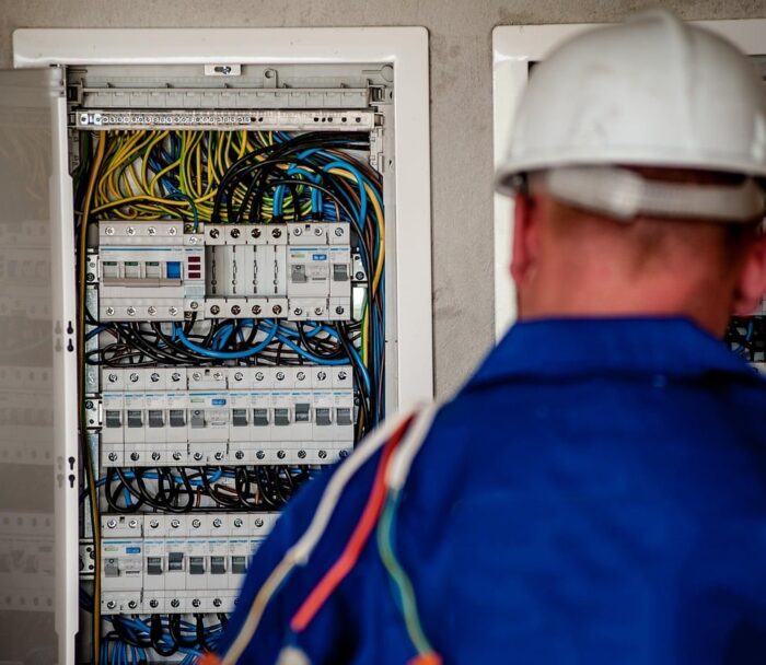 Elektriker mit Schutzhelm vor einem geöffneten Stromverteiler